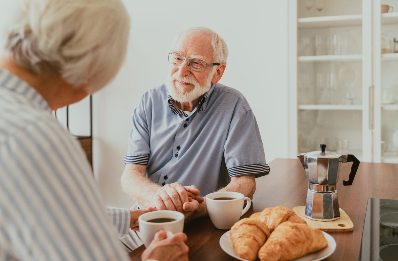 An older couple reminisces together over coffee and a plate of croissants in independent living
