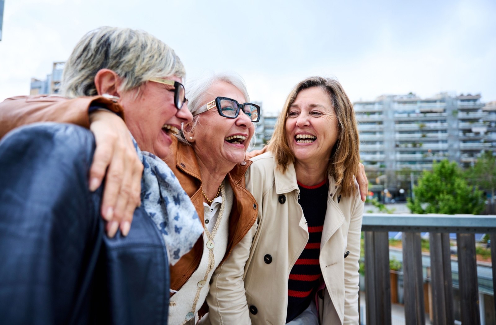 A retiree and their two friends laugh and embrace while outdoors in an urban environment.