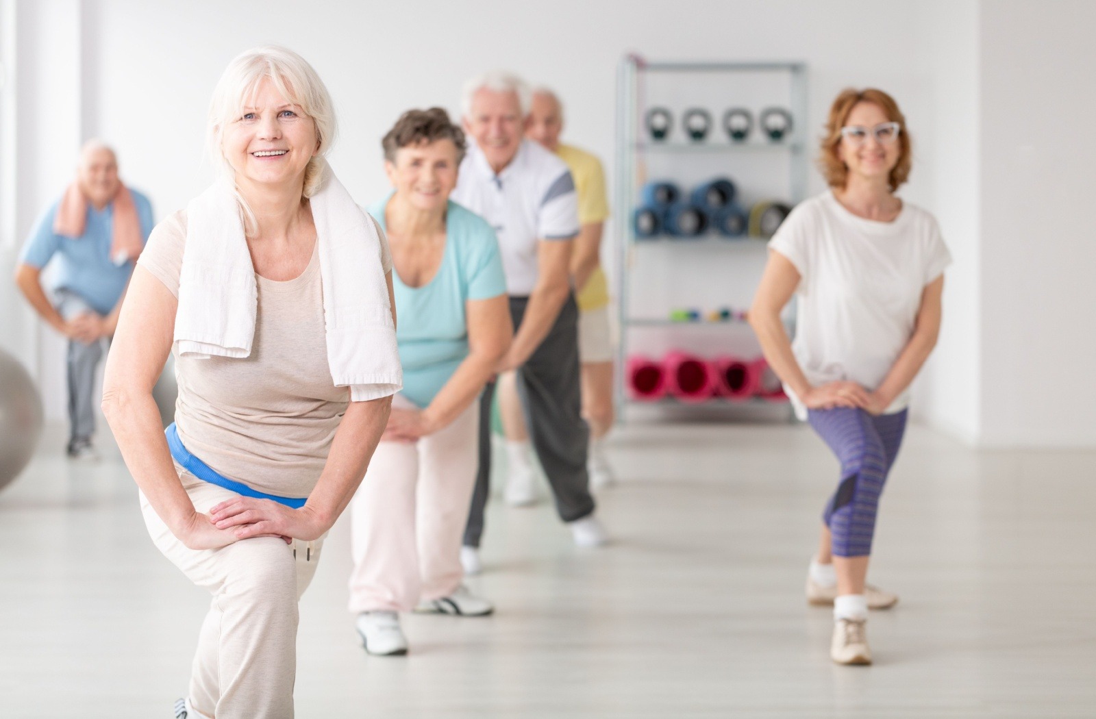 A group of active older adults participate in an exercise class in a well-lit studio at a senior living community.