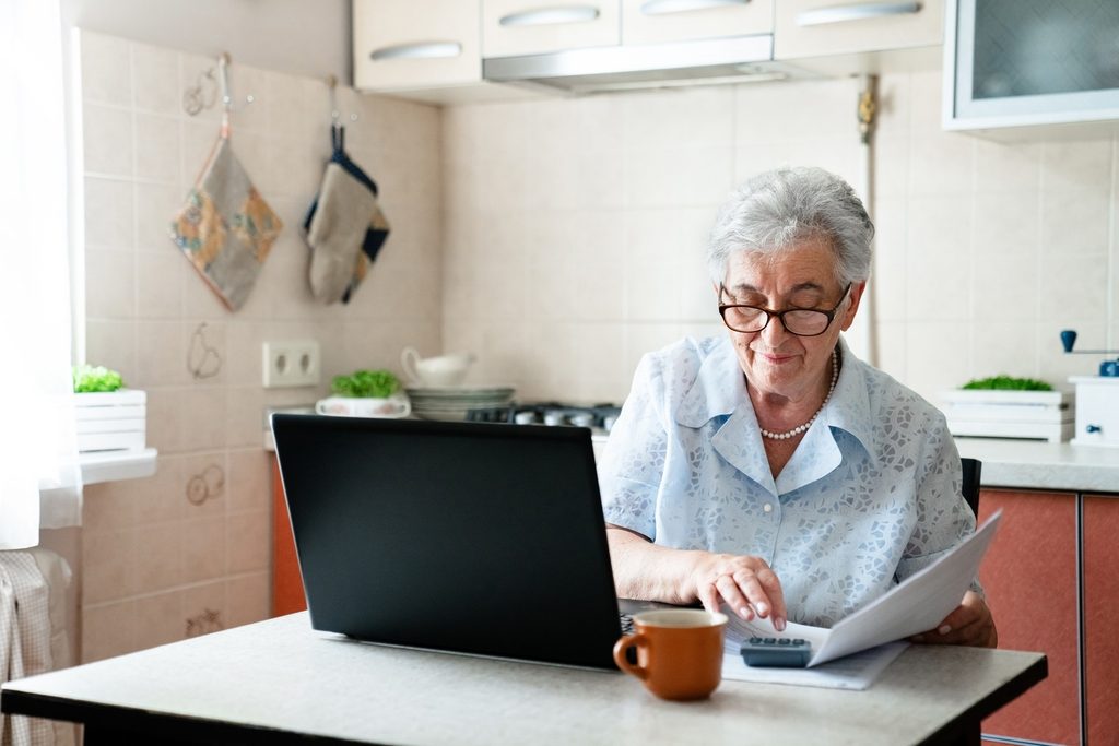 Senior female resident paying utility bills in the kitchen. Personal budgeting, financial literacy, retirement savings, pension plan, getting ready for assisted living