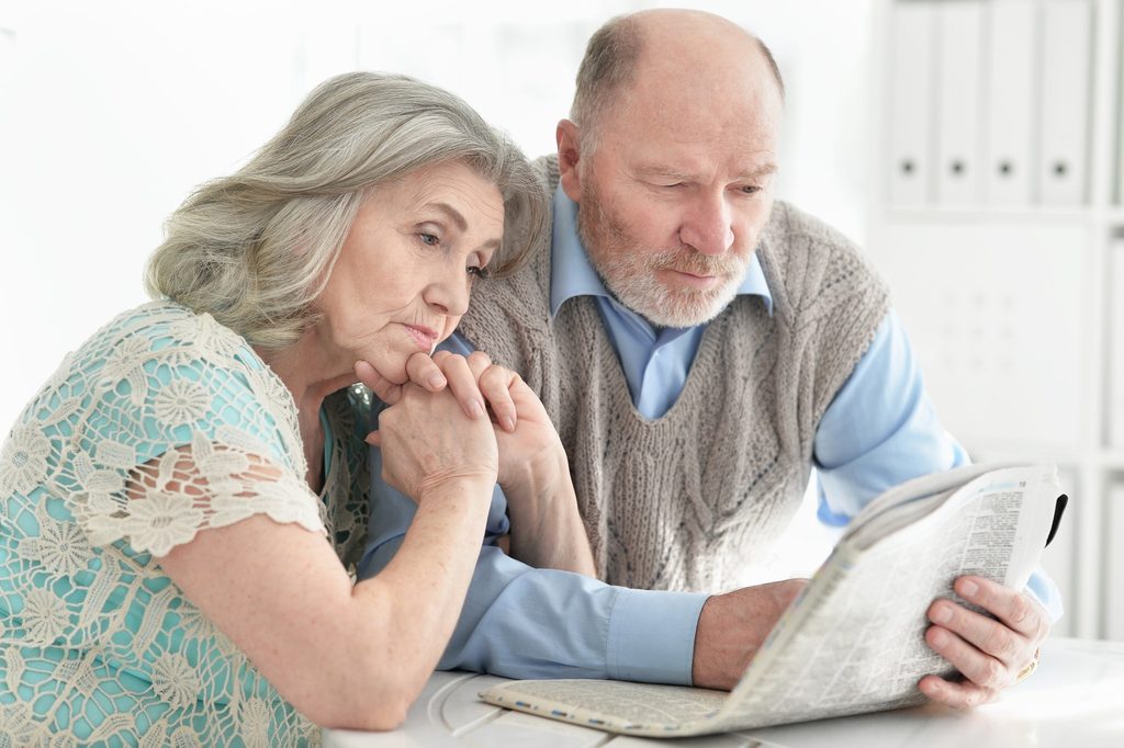 Close-up portrait of a senior couple reading the newspaper together at home as a routine